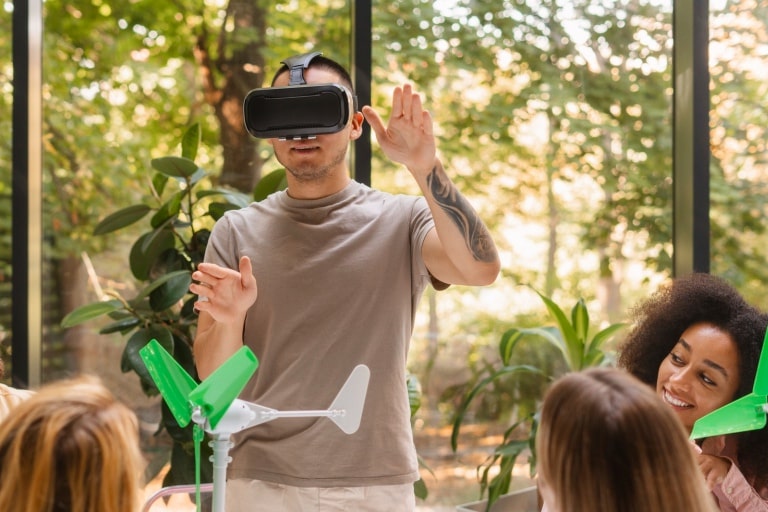 A boy with VR reality glasses doing hand gestures in a team setting with 3 girls